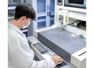Junge Arbeitskraft im weißen Kittel und mit Maske bedient einen Computer in einer modernen Produktionsstätte in Südkorea