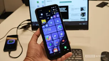 Смартфон NexPhone в руке на фоне ноутбука с открытыми окнами