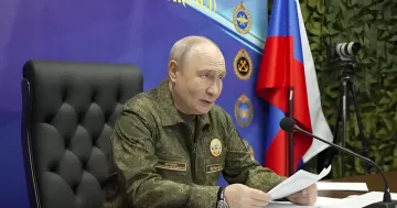 Vladimir Putin in camouflage attire speaking against the background of the official flag