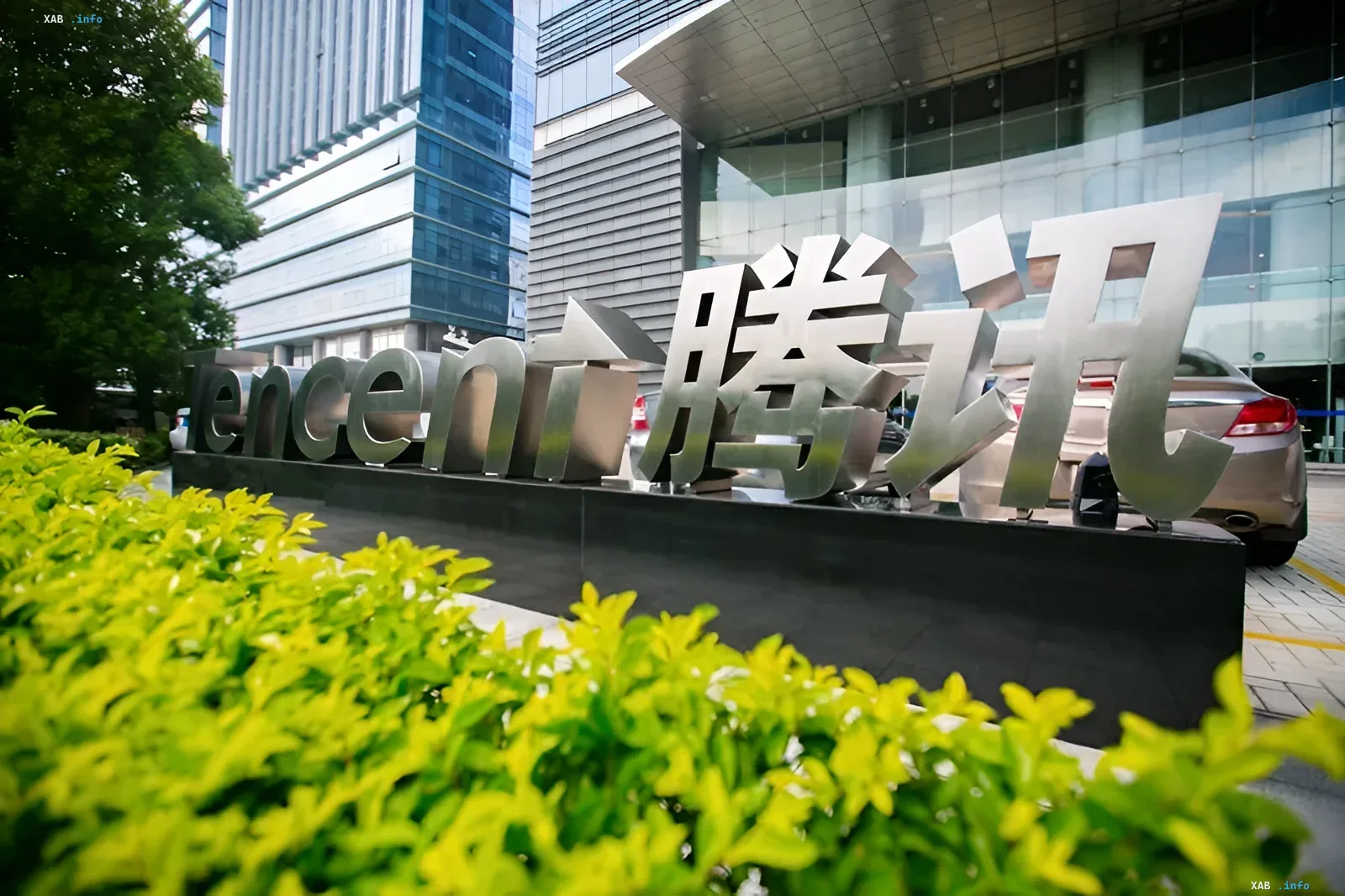 Корпоративный логотип Tencent на фоне современного небоскреба и зелени