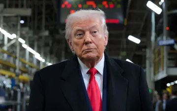 US President Donald Trump wearing a coat and red tie at a factory