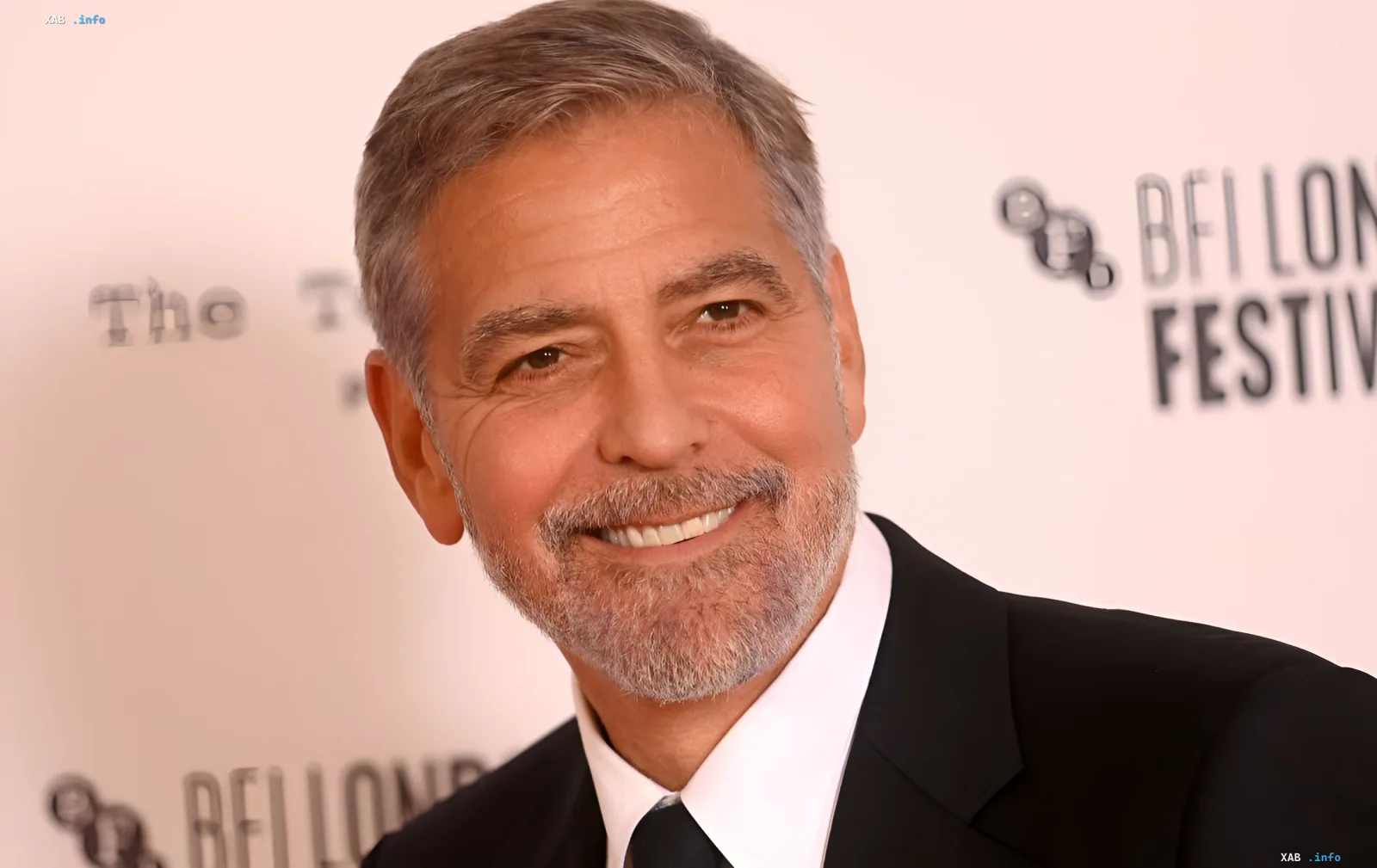 Hollywood actor George Clooney smiling at a presentation against a light wall with lettering
