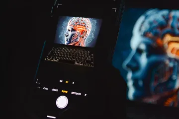 Смартфон фотографирует экран ноутбука с изображением человеческого мозга и ИИ