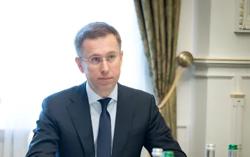 Ein Mann im klassischen Anzug und mit Brille sitzt an einem Tisch bei einer Regierungssitzung