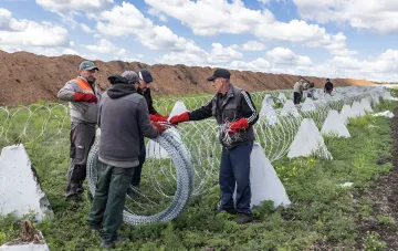 Рабочие в защитной экипировке устанавливают противотанковые ежи и колючую проволоку на оборонительном рубеже