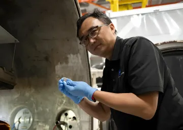 A NASA employee in protective gloves holding a prototype SPEARS solid-state battery in a laboratory