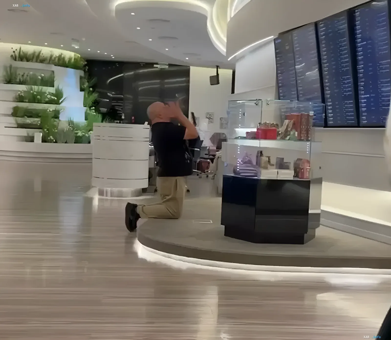 Мужчина в черной футболке стоит на коленях и молится в пустом терминале аэропорта