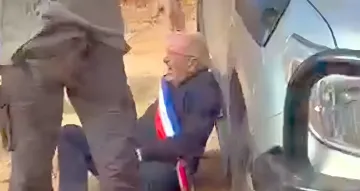 Пожилой человек с лентой в цветах французского флага лежит на земле рядом с автомобилем после нападения поселенцев
