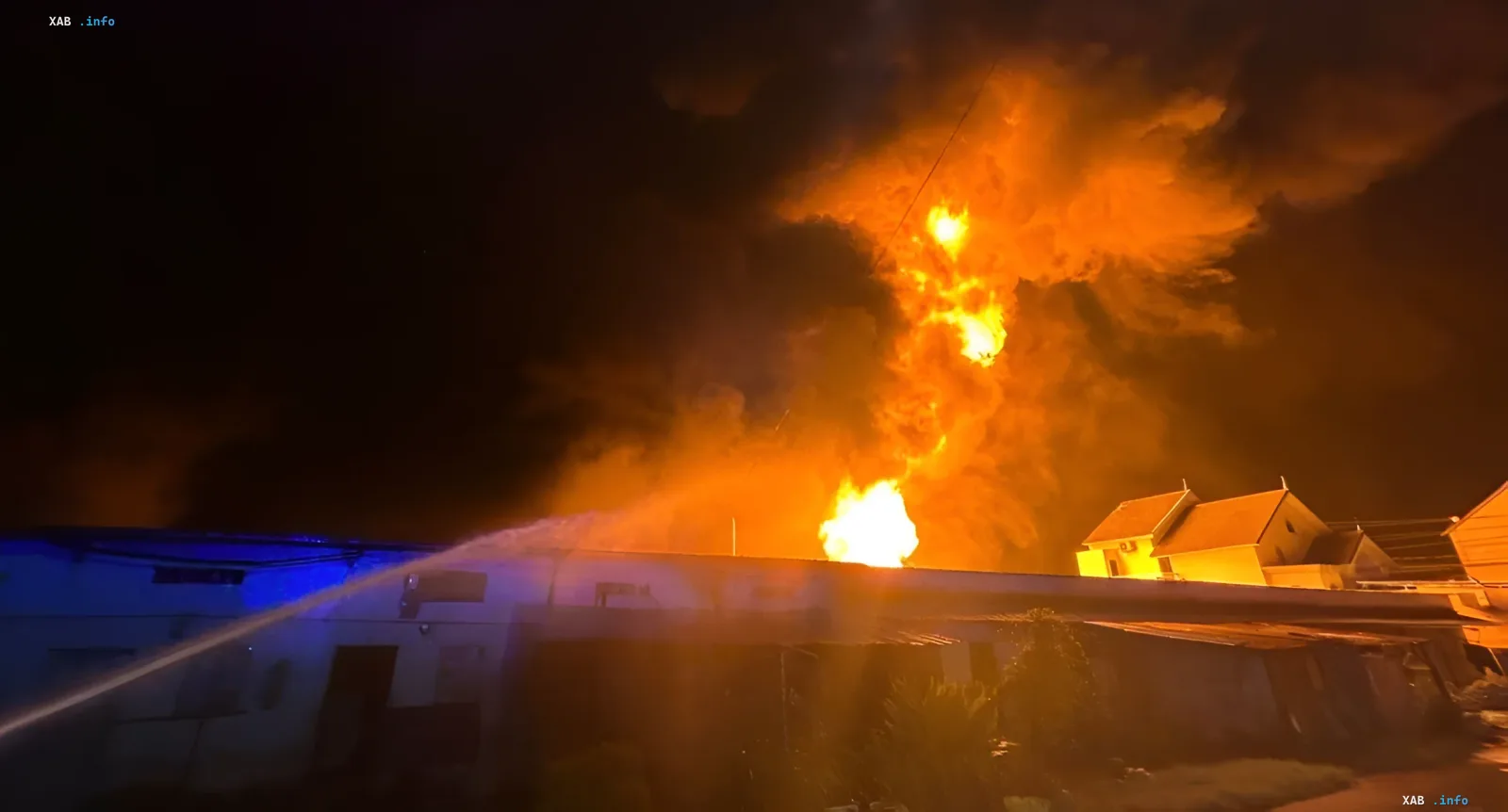 Nighttime fire at a military base with bright flames and a fire hose