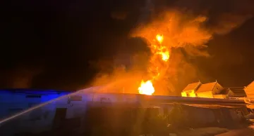 Nächtlicher Brand auf einem Militärstützpunkt mit hellen Flammen und einem Feuerwehrschlauch