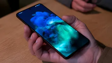 Рука тримає смартфон Samsung Galaxy з увімкненим яскравим абстрактним синьо-зеленим екраном