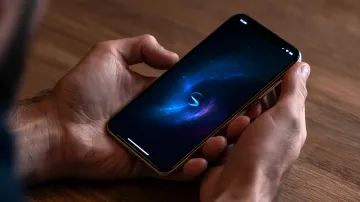 Eine Person hält ein Smartphone mit einer Galaxiengrafik auf dem Bildschirm an einem Holztisch