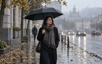 Жінка з чорною парасолькою йде вологою осінньою вулицею міста під дощем
