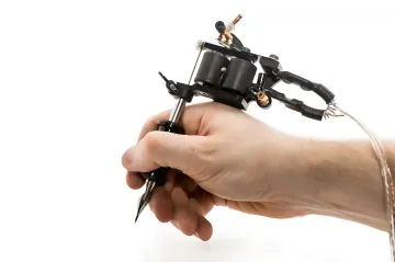 Hand holding a tattoo machine in close-up on a white background