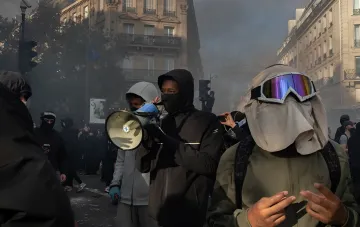 Protesters in masks and protective goggles with a megaphone amid smoke and Parisian streets during riots