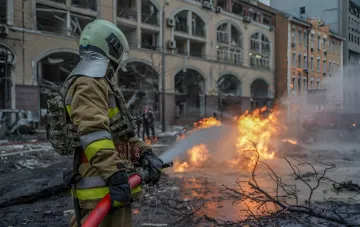A firefighter in protective gear puts down a fire after shelling in a residential area of Kyiv