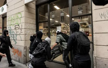 Hooded protesters attacking a shop window in central Milan during mass riots