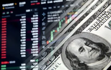 Trading charts on a monitor and a stack of US dollars with Franklin's portrait