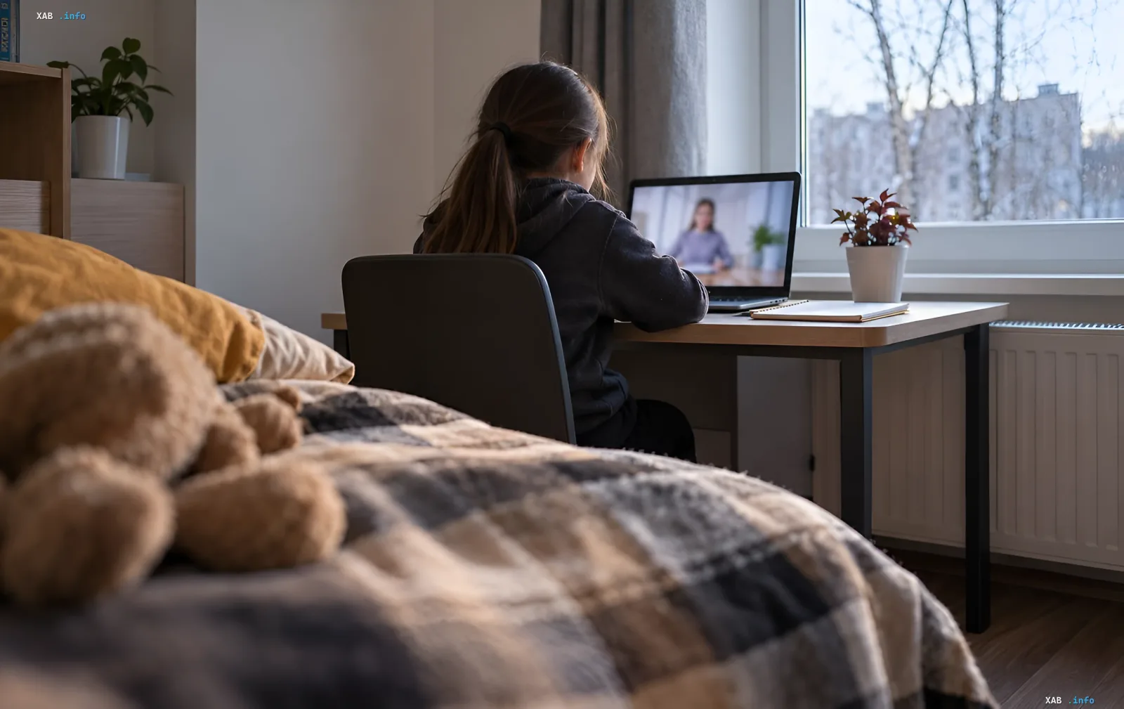 A child sits at a desk and studies on a laptop in a room by the window