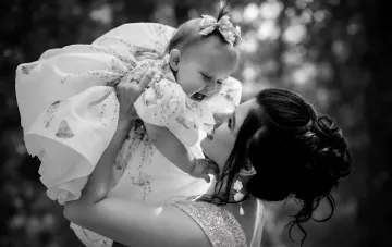 A mother tenderly holding her little daughter in a festive dress outdoors