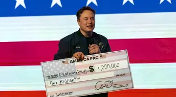 Elon Musk hält einen symbolischen Scheck über eine Million US-Dollar vor einer US-Flagge