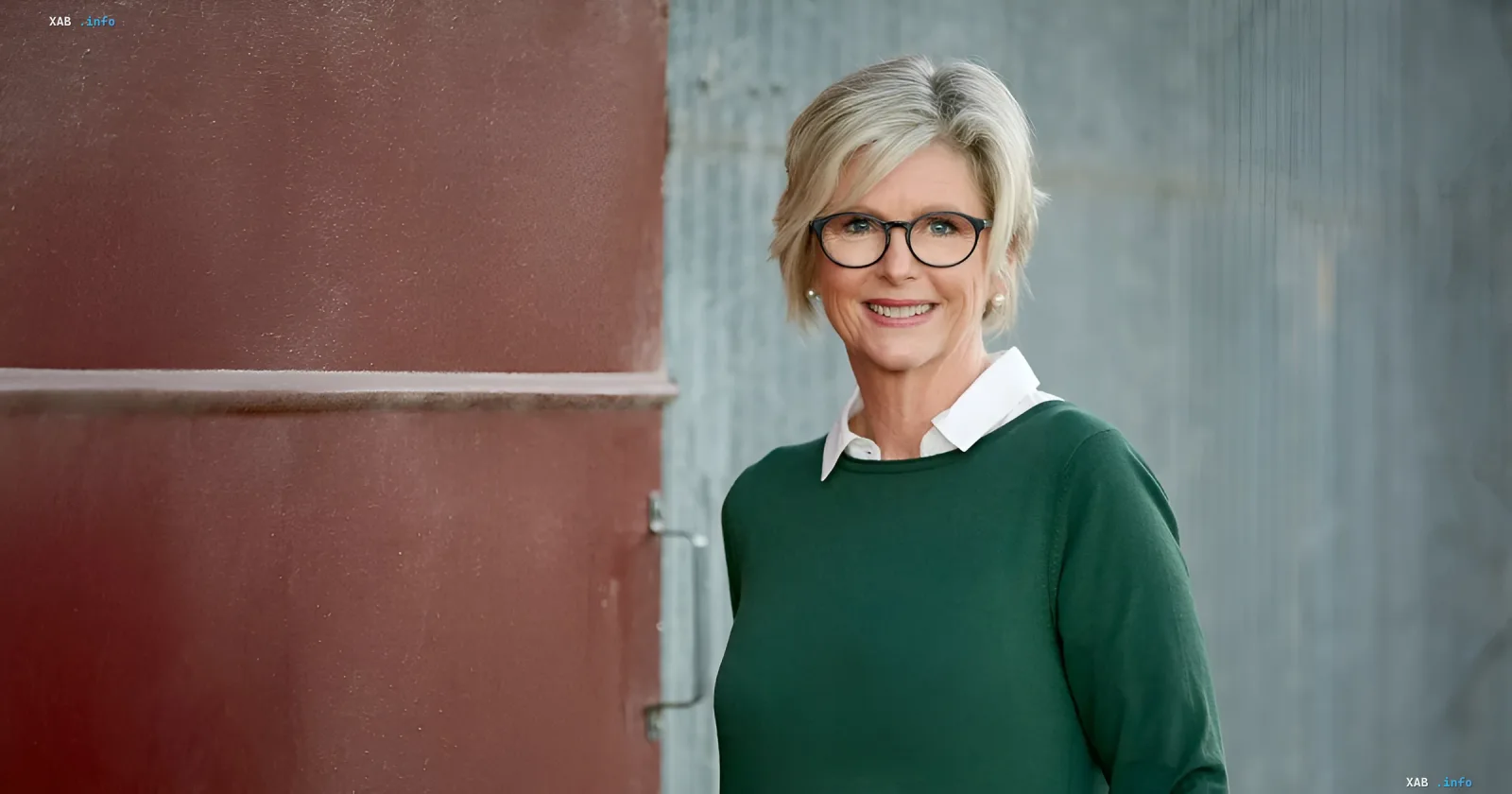Frau mit Brille und grünem Pullover steht vor einer Wand
