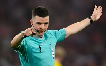Football referee in a turquoise kit pointing his hand on the pitch during a match