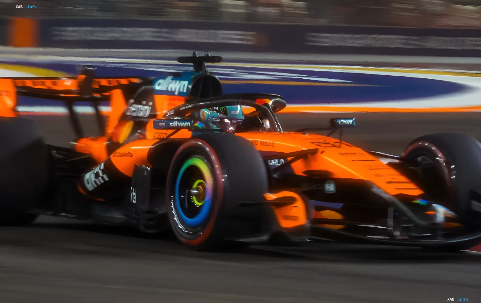 Bright orange McLaren racing car speeding along a night Formula 1 track