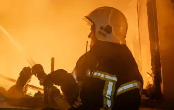 Firefighter in protective helmet extinguishing a massive fire at a destroyed enterprise