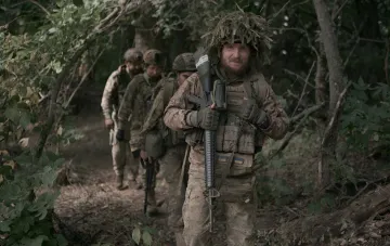 A group of Ukrainian soldiers in camouflage with weapons walking through a forest during training