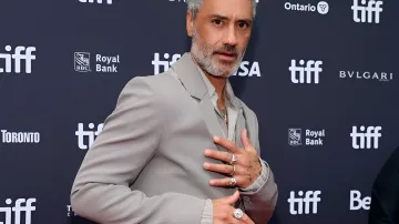 Director Taika Waititi wearing an elegant grey suit on a film festival red carpet