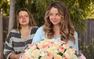 Ukrainian blogger Vlada Rogovenko holding a large bouquet of flowers next to an upset woman against a background of nature.