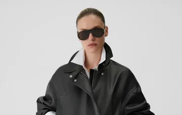Model wearing sunglasses and a black leather jacket over a white shirt
