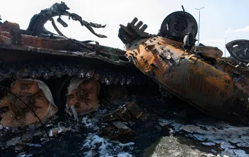 Burned Russian armored vehicles and a destroyed tank on a ruined road after battles