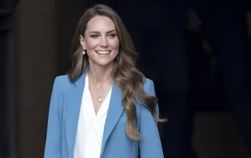 Kate Middleton wearing a blue blazer and white blouse smiling at an official event
