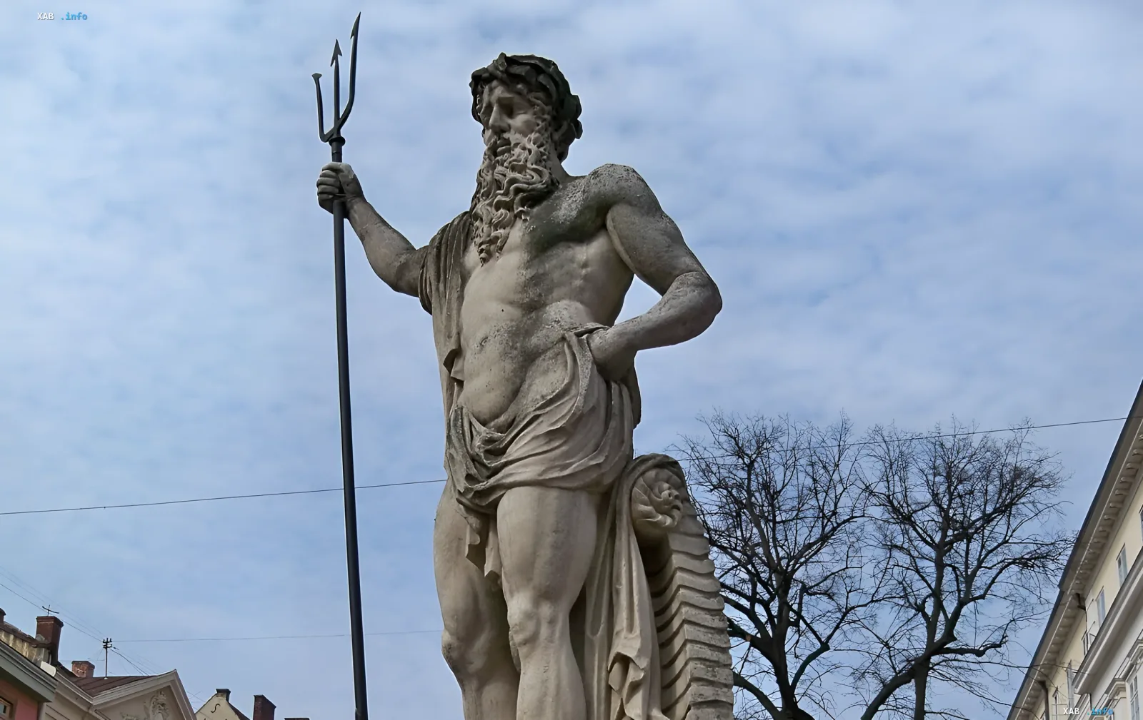 Stone statue of the god Neptune with a trident against a cloudy sky in Lviv