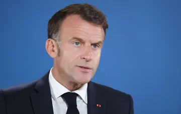 French President Emmanuel Macron speaking at a press conference against a blue background