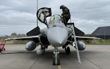 Military pilot climbing a ladder into the cockpit of a Rafale multirole fighter jet at an airfield