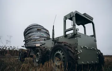 Ground military robot with a barbed wire coil on the battlefield