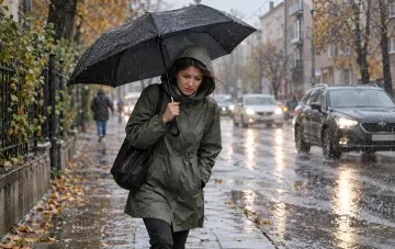 Жінка під чорною парасолькою йде мокрою від дощу вулицею осіннього міста