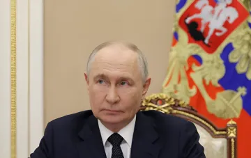 Vladimir Putin sitting at a table against the background of the Russian national flag