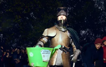 A man in medieval plate armor sits on a bright green Lime rental e-bike in a London park