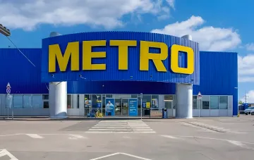 Facade of the Metro supermarket building with blue walls and a yellow sign under a cloudy sky