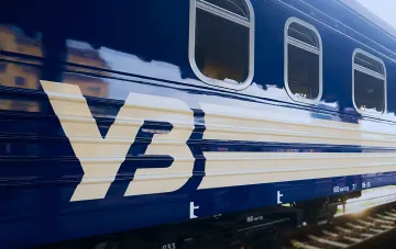 Синій пасажирський вагон Укрзалізниці з білими смугами та написом УЗ на тлі залізничної колії