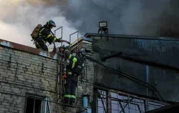 Firefighters extinguish a burning factory building, clearing the aftermath of a nighttime strike