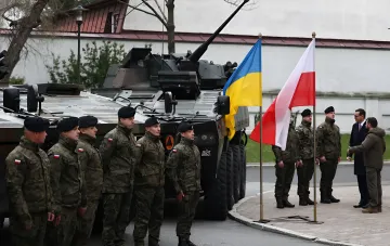 Ukrainian and Polish flags next to armored vehicles and military personnel during an official meeting