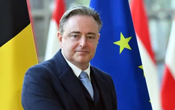 Премьер-министр Бельгии Барт де Вевер на фоне флагов Бельгии и ЕС во время выступления