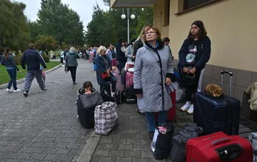 Люди с багажом стоят в очереди, ожидая отъезда, что символизирует демографический кризис и миграцию.