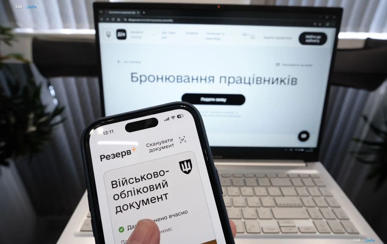 Смартфон с открытым электронным военно-учетным документом на фоне ноутбука с сайтом бронирования работников