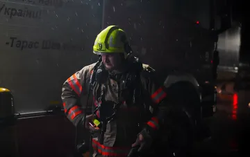 Пожарный в защитной каске и форме стоит у пожарной машины ночью во время дождя в Киеве